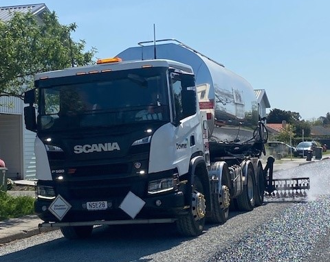 Truck spraying small chip stones onto bitumen glue.